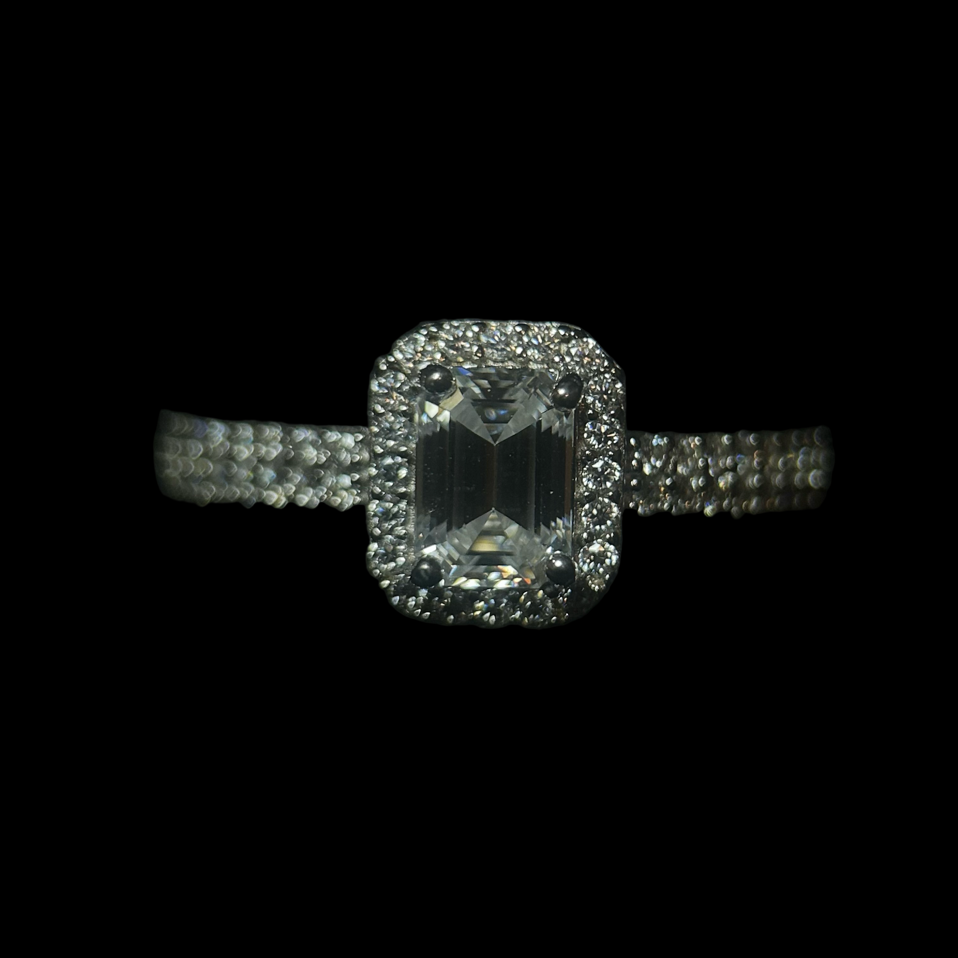 Diamond ring with a rectangular stone and halo on a black background, branded 'CRUDDA'.