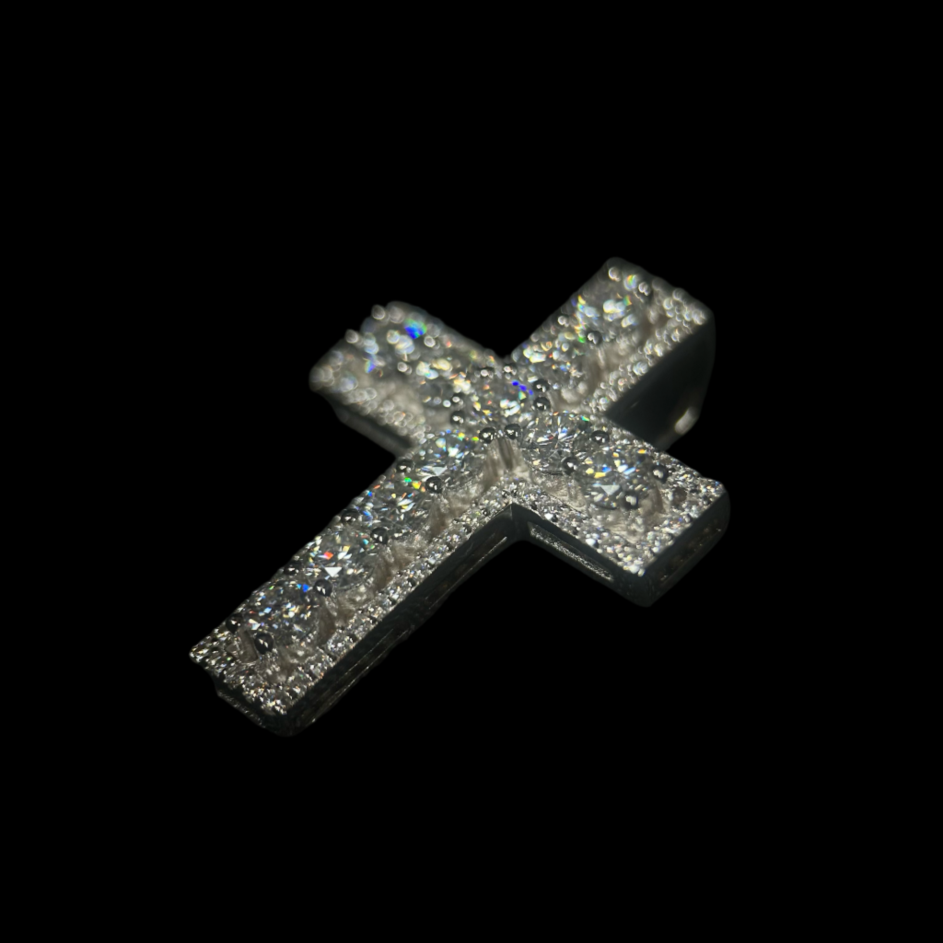 Silver cross pendant with sparkling stones on a black background, branded 'CRUDDA'.
